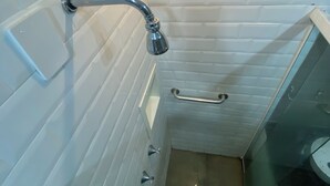 Ein Badezimmer mit weißen Fliesen, einer Duschkabine aus Glas, einem Handbrausekopf und einer Haltestange.