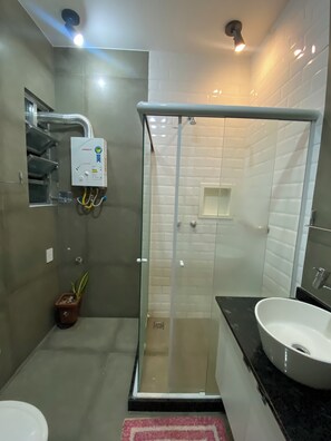 Ein modernes Badezimmer mit einer gläsernen Dusche, einem weißen Waschbecken und einem kleinen Topfpflanzen.