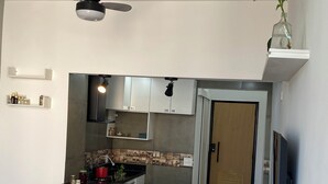 Eine kompakte Küche mit einer zentralen Kochinsel, zwei Barhocker, einem Deckenventilator und einem an der Wand befestigten Fernseher.