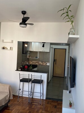 Eine kompakte Küche mit einer zentralen Kochinsel, zwei Barhocker, einem Deckenventilator und einem an der Wand befestigten Fernseher.