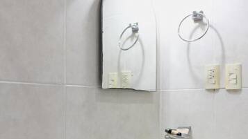 Un baño con inodoro, lavabo con dispensador de jabón y dos anillos para toallas en la pared.