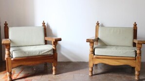 Deux chaises en bois, dotées d’un siège et d’un dossier rembourrés, sont placées contre un mur uni.