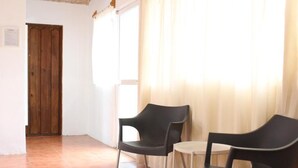 Une pièce avec deux chaises noires, une petite table ronde, une porte en bois et une fenêtre ornée de rideaux légers.