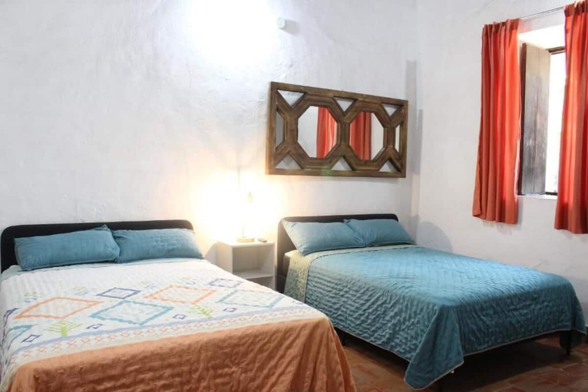 Two single beds with headboards, a wall-mounted decorative piece, and a window with red curtains.
