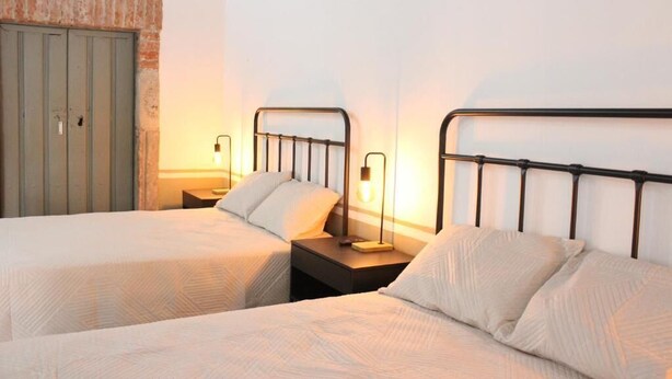 Une chambre d’hôtel avec deux lits simples, une table de chevet avec une lampe, une armoire et un mur en briques.