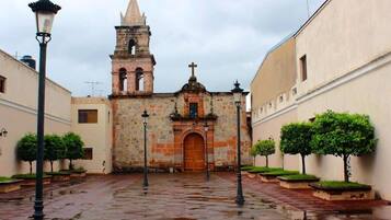 A historic church with a bell tower, a courtyard with a wet pavement, and lamp posts.
