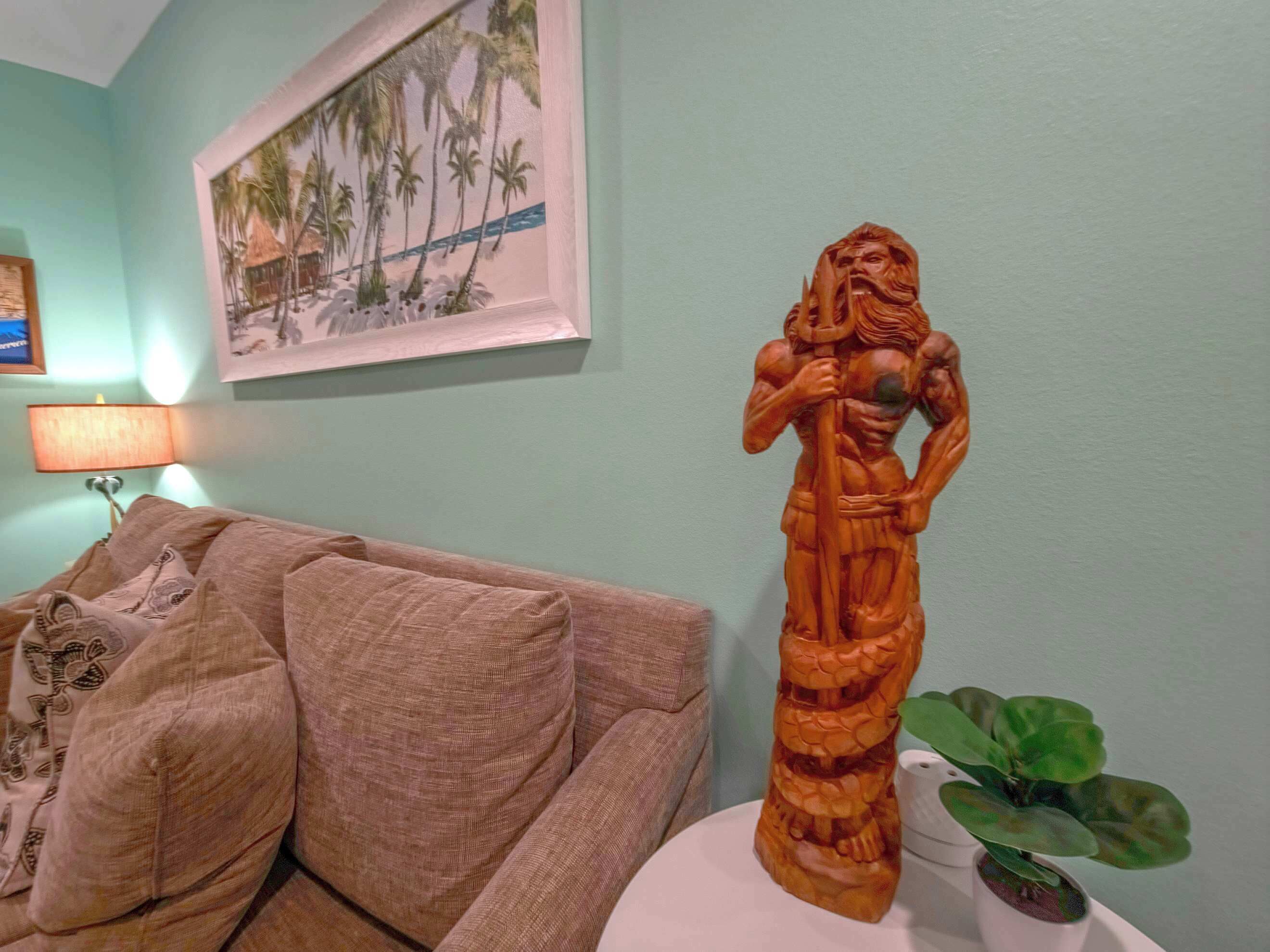 Et værelse med en sofa, et indrammet billede, en træskulptur og en potteplante.