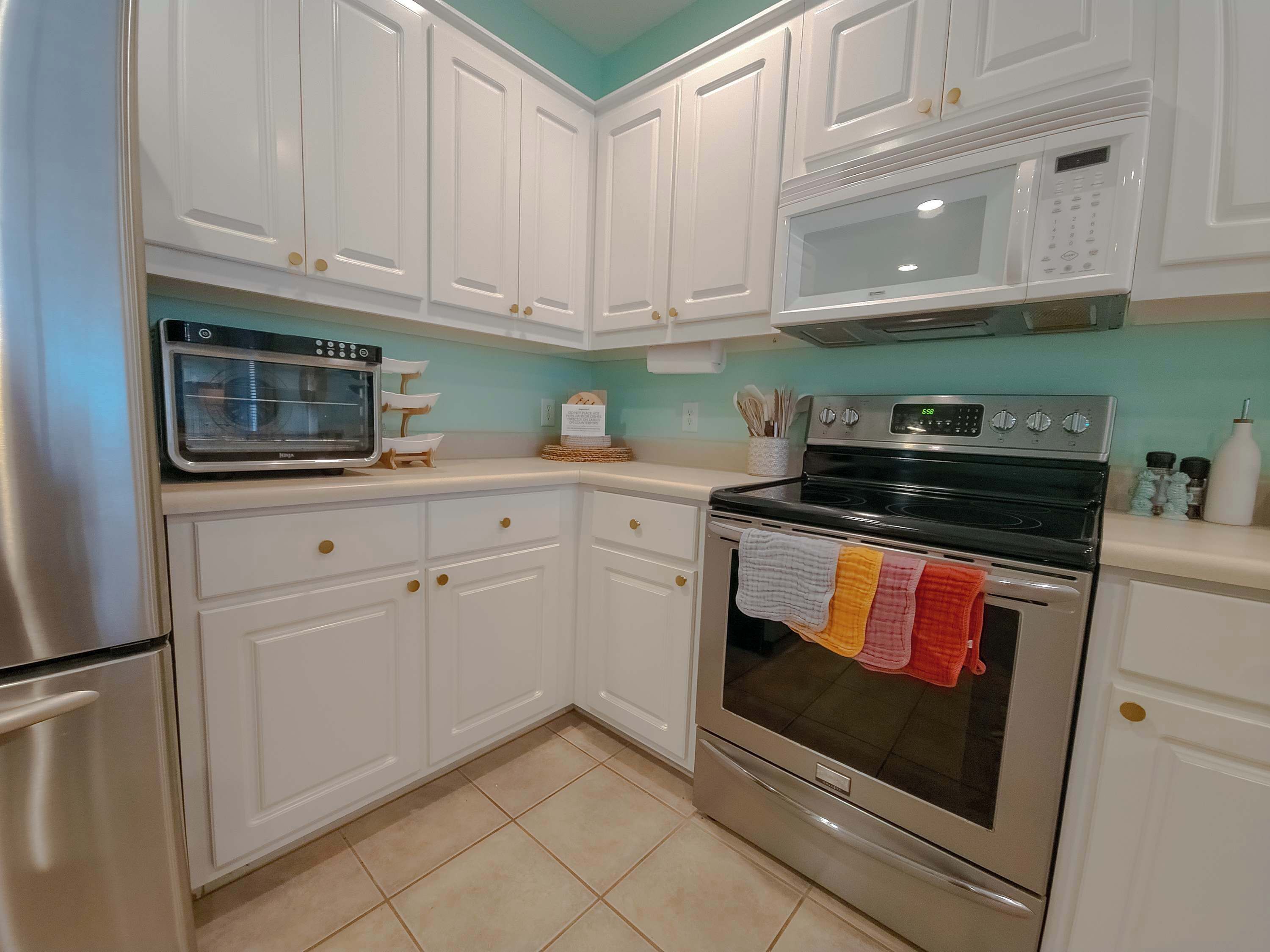 Una cocina con gabinetes blancos, microondas, estufa y refrigerador.