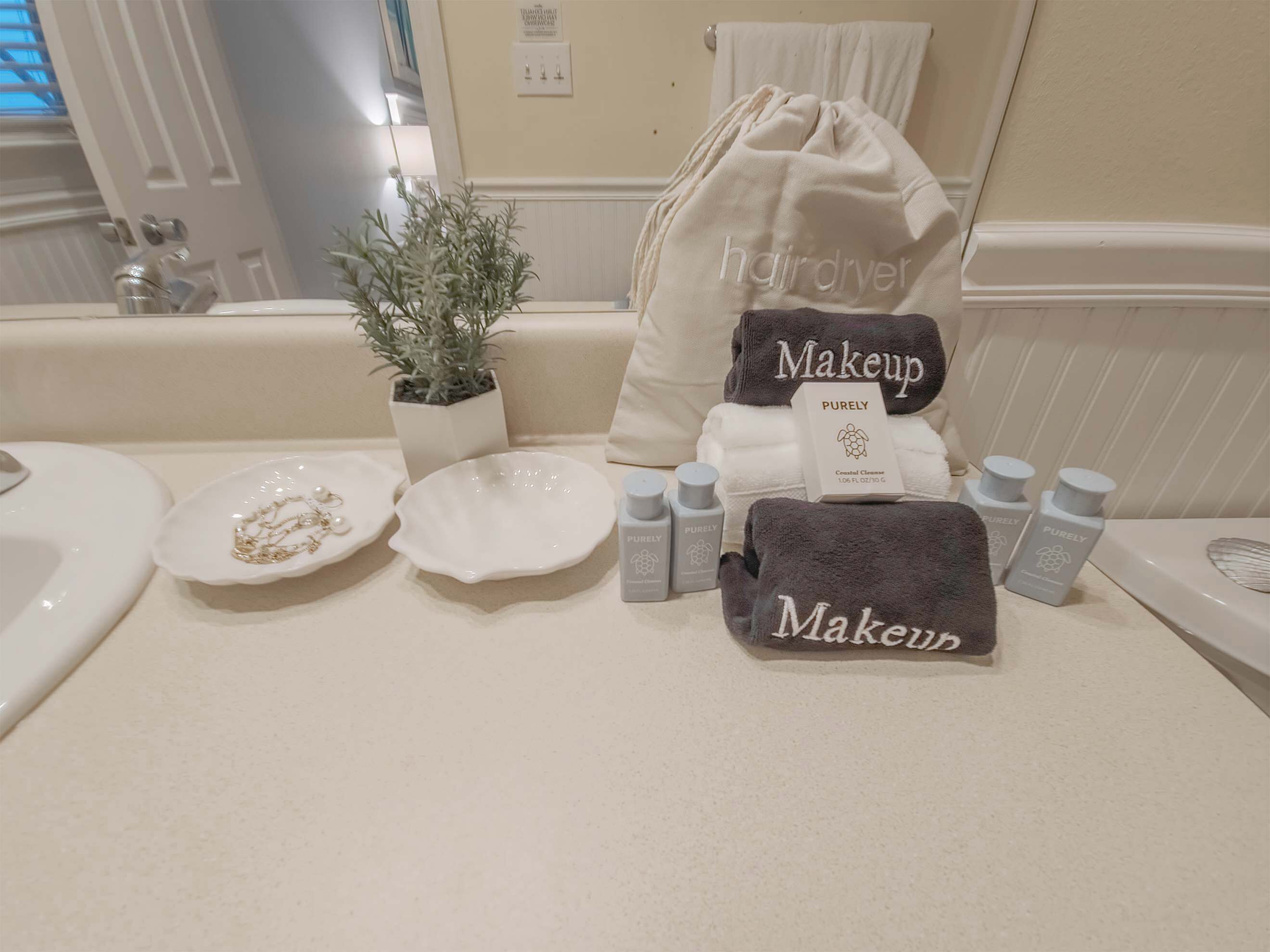 Un tocador de baño con un lavabo, una planta en maceta, un neceser de maquillaje, una toalla de maquillaje y varias botellas de productos para el cuidado de la piel.
