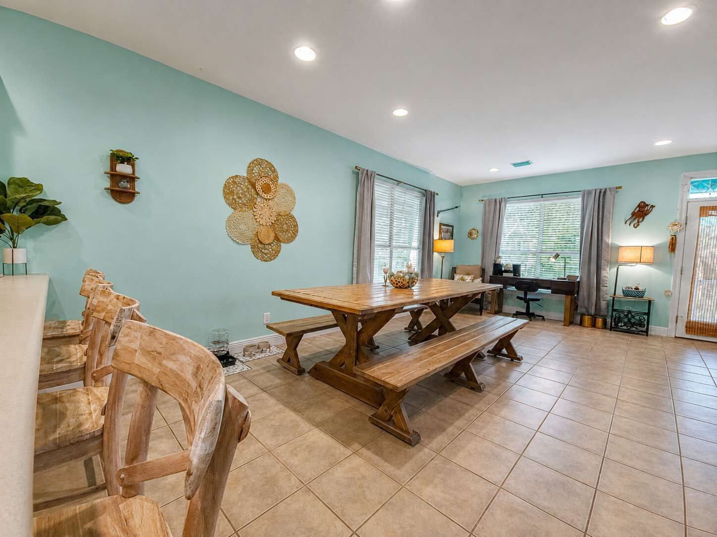 Un coin repas avec une table et des bancs en bois, un élément décoratif fixé au mur et une fenêtre avec des rideaux.
