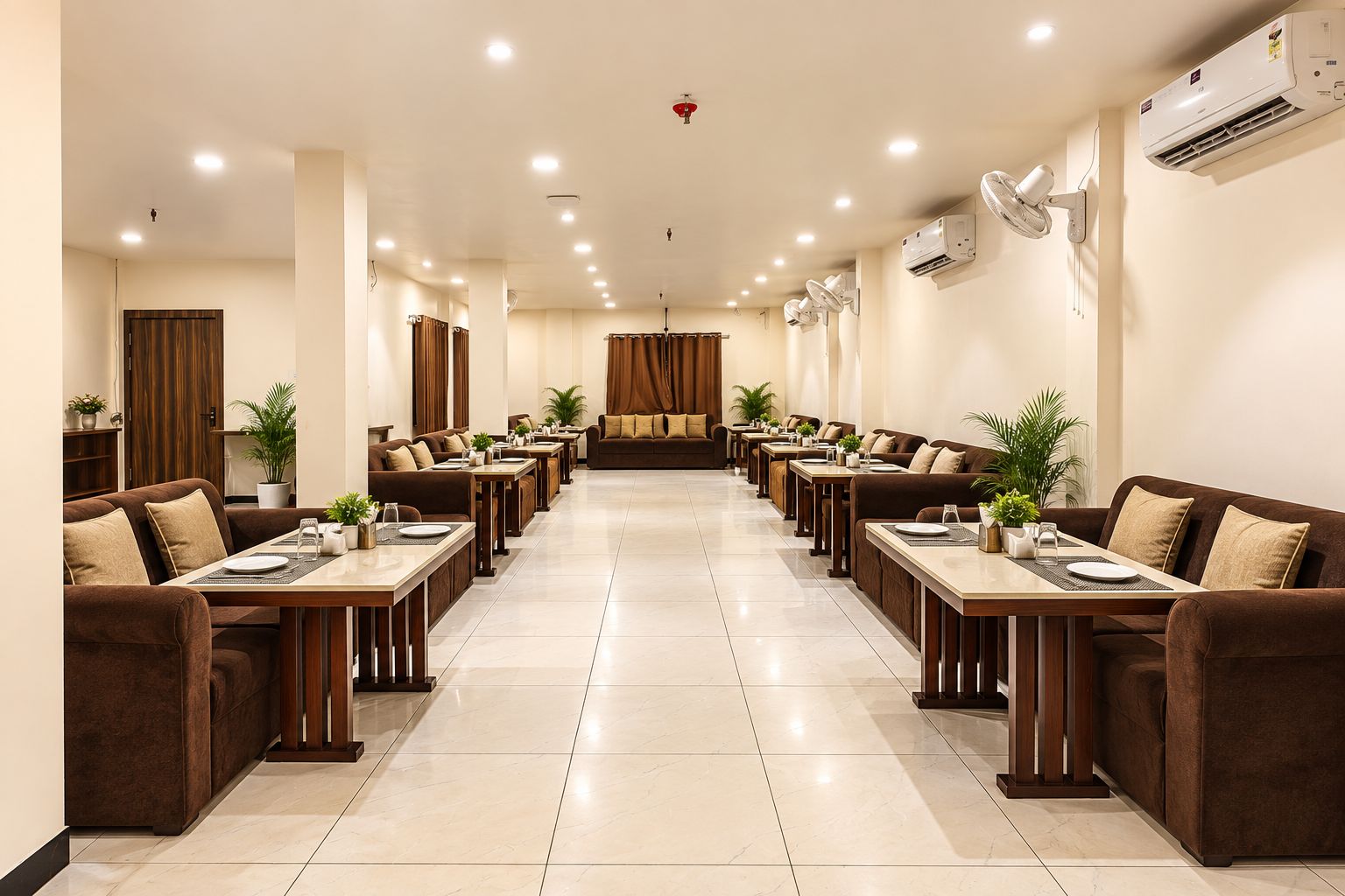 Un comedor de hotel con varias mesas y sofás, unidades de aire acondicionado e iluminación en el techo.