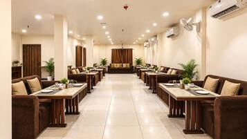 Un comedor de hotel con varias mesas y sofás, unidades de aire acondicionado e iluminación en el techo.