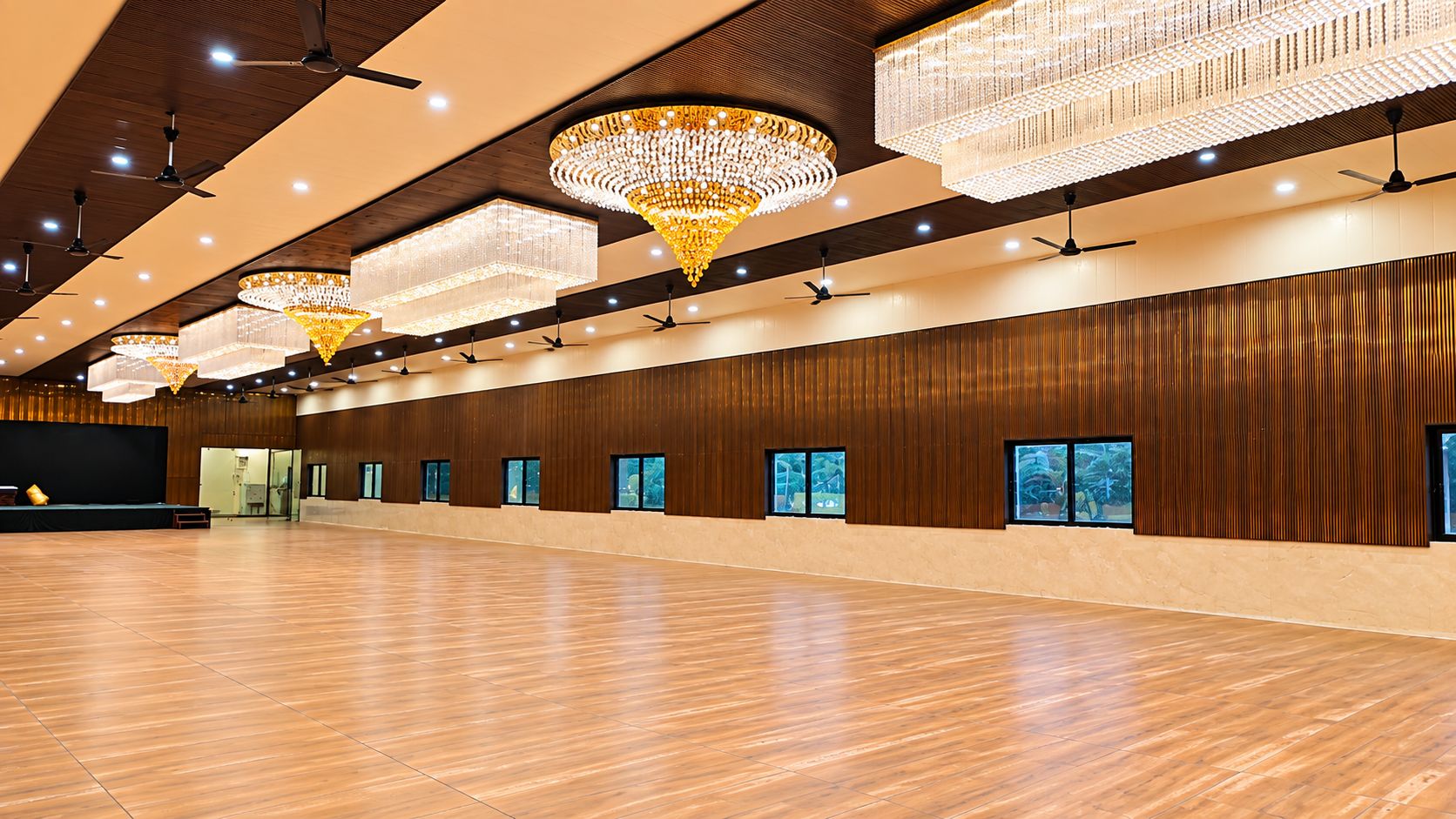 Un amplio salón con múltiples candelabros, paneles de madera y un escenario.