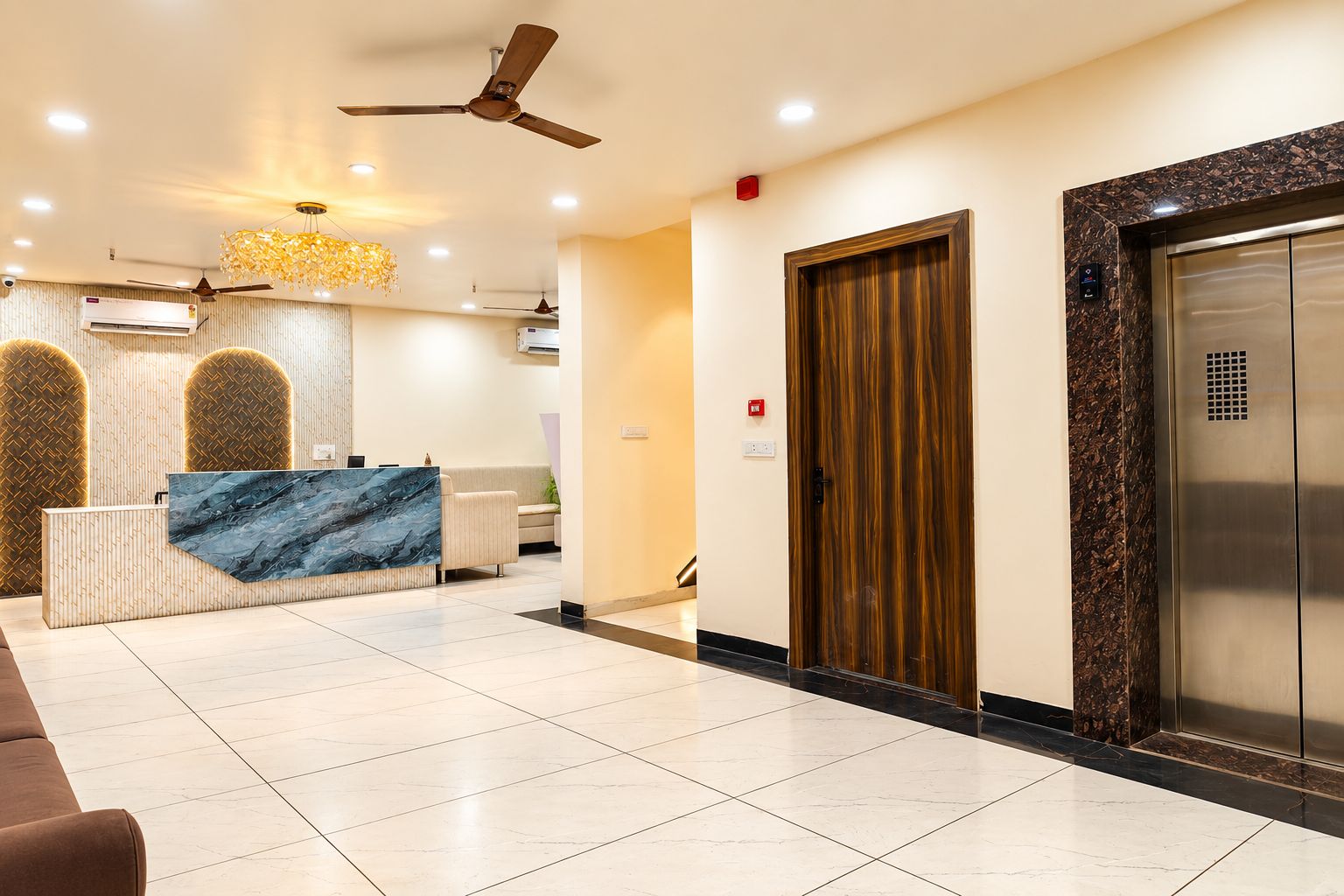 Un área de recepción de hotel con un mostrador de mármol, un ventilador de techo y una puerta de madera.