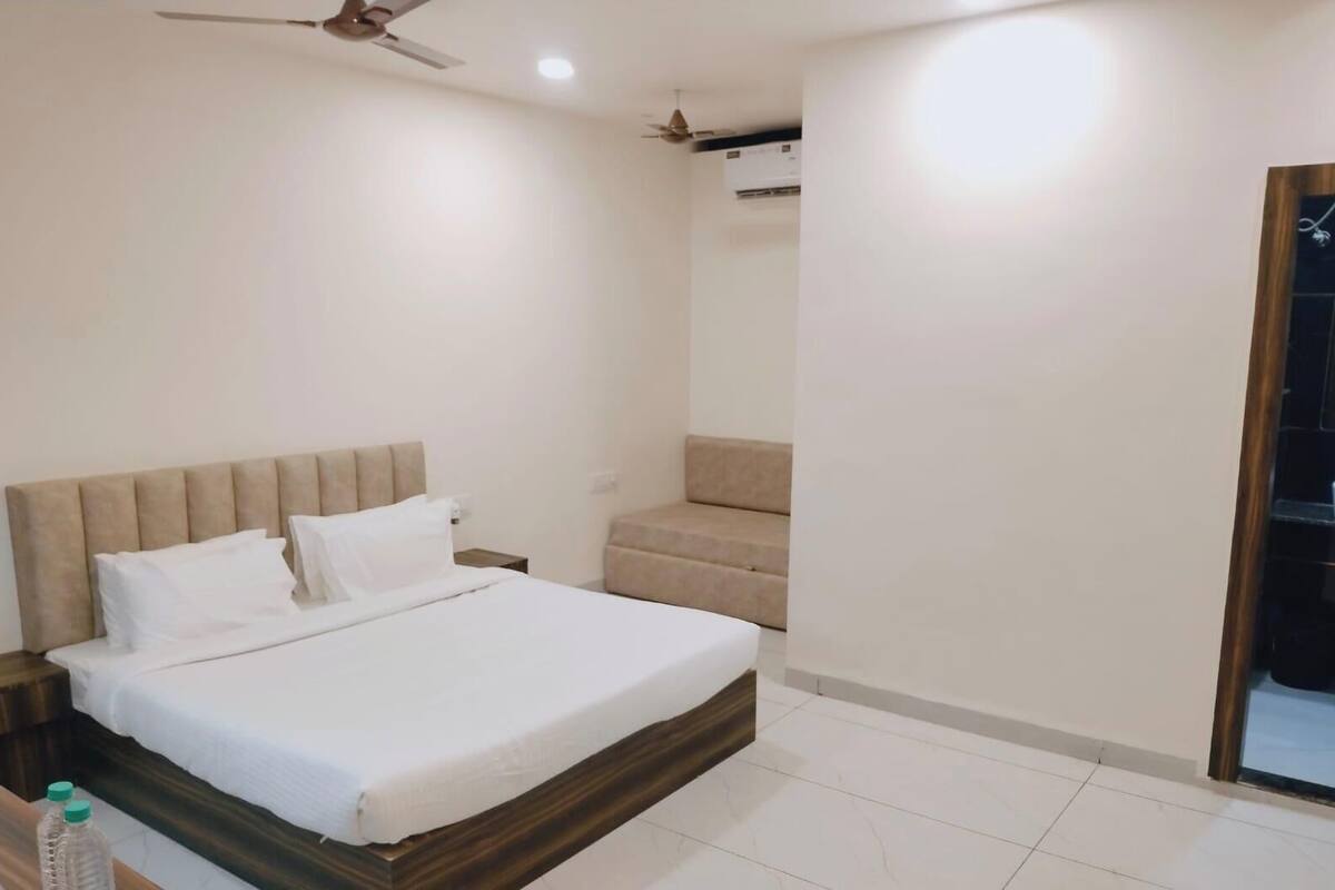 A bedroom with a bed, a nightstand, a ceiling fan, an air conditioning unit, and a small seating area.