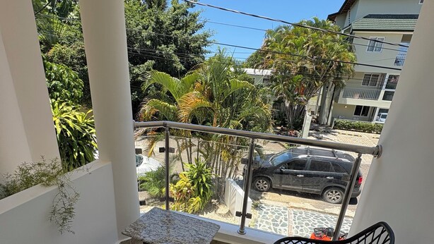 A balcony with two chairs, a small table, and a view of a street with cars and buildings. - Delightful 1-bedroom apartment with AC in Sosua (Sosua)