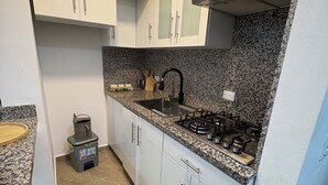 A kitchen with white cabinets, a granite countertop, a gas stove, and a sink. - Delightful 1-bedroom apartment with AC in Sosua (Sosua)