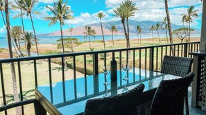 Ein Balkon mit Tisch und Stühlen, der auf eine Küstenlandschaft mit Palmen und Bergen blickt.