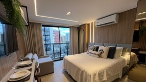Quarto de hotel moderno com uma cama grande, área de refeições e vista para a cidade.