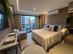 Ein modernes Hotelzimmer mit einem großen Bett, einer Essecke und Blick auf die Stadt.
