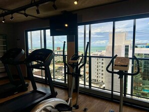 Ein Fitnessraum mit Laufbändern, Crosstrainern und einem stationären Fahrrad, mit Blick auf die Stadt durch große Fenster.