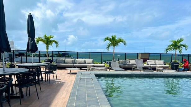 Área de piscina no terraço com espreguiçadeiras, mesas e guarda-sóis, com vista para um corpo de água.