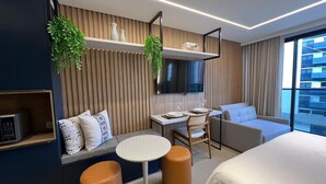 Quarto de hotel moderno com cama, área de refeições, televisão e vista para a cidade.
