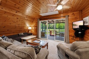 A cozy living room with wooden walls, a ceiling fan, a sofa, a coffee table, and a view of a patio with outdoor furniture.