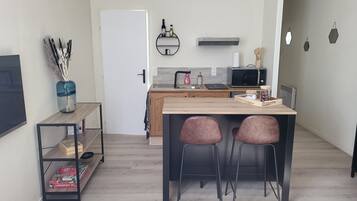 Une cuisine moderne avec une table en bois, deux chaises, un four à micro-ondes et une petite étagère avec des bouteilles.
