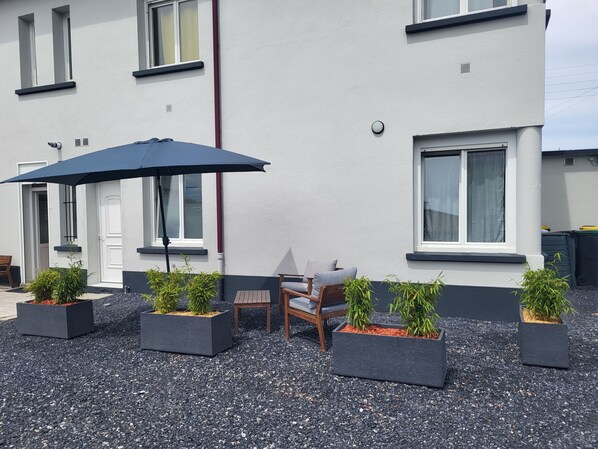 A building with a white exterior, black window frames, and a door. There are outdoor seating arrangements with a table and chairs, and several potted plants. - Cosy bubble with private terrace and parking area Bed linen and towels provided (Tarbes)