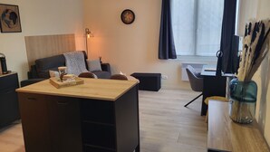 Ett modernt vardagsrum med ett soffbord i trä, en soffa, ett skrivbord och en stol. Det finns en klocka på väggen och ett fönster med gardiner.