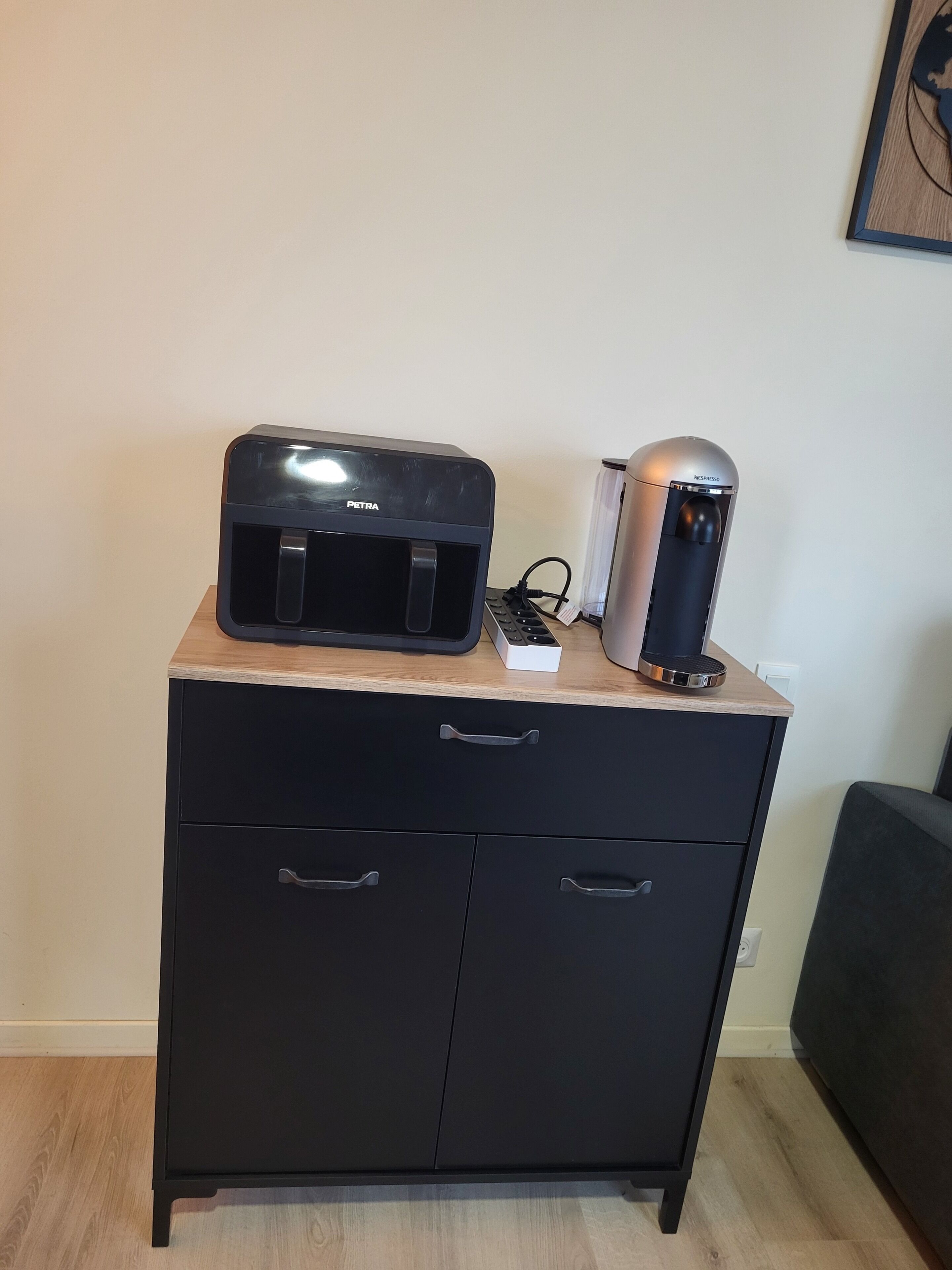 Un meuble noir avec deux tiroirs et une petite machine à café posée sur le dessus.