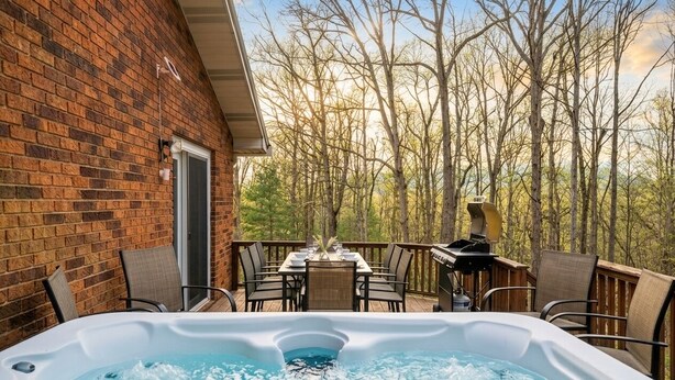 A hot tub on a deck with a brick wall and a table with chairs. - New River Gorge - Private Acre, Pet-Friendly, Dome, Hot Tub, Sauna, Firepit (Oak Hill)