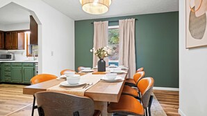 A dining area with a wooden table, orange chairs, a vase with flowers, and a view of a green exterior through a window. - New River Gorge - Private Acre, Pet-Friendly, Dome, Hot Tub, Sauna, Firepit (Oak Hill)