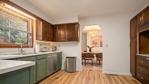 A kitchen with wooden cabinets, a sink, and a dining area with chairs and a table. - New River Gorge - Private Acre, Pet-Friendly, Dome, Hot Tub, Sauna, Firepit (Oak Hill)
