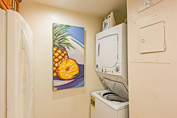 Un cuarto de lavandería con lavadora, un cuadro de piña y un refrigerador.