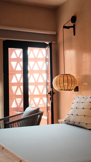 Ein Zimmer mit einem Bett, einem Sessel, einer Wandlampe und einer Tür mit geometrischem Muster.