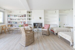 Ein geräumiges Wohnzimmer mit Rattanmöbeln, einem Kamin und einem Bücherregal voller Bücher.