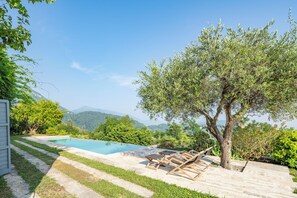 Ein Poolbereich mit Liegestühlen, einem Baum und Blick auf Berge.