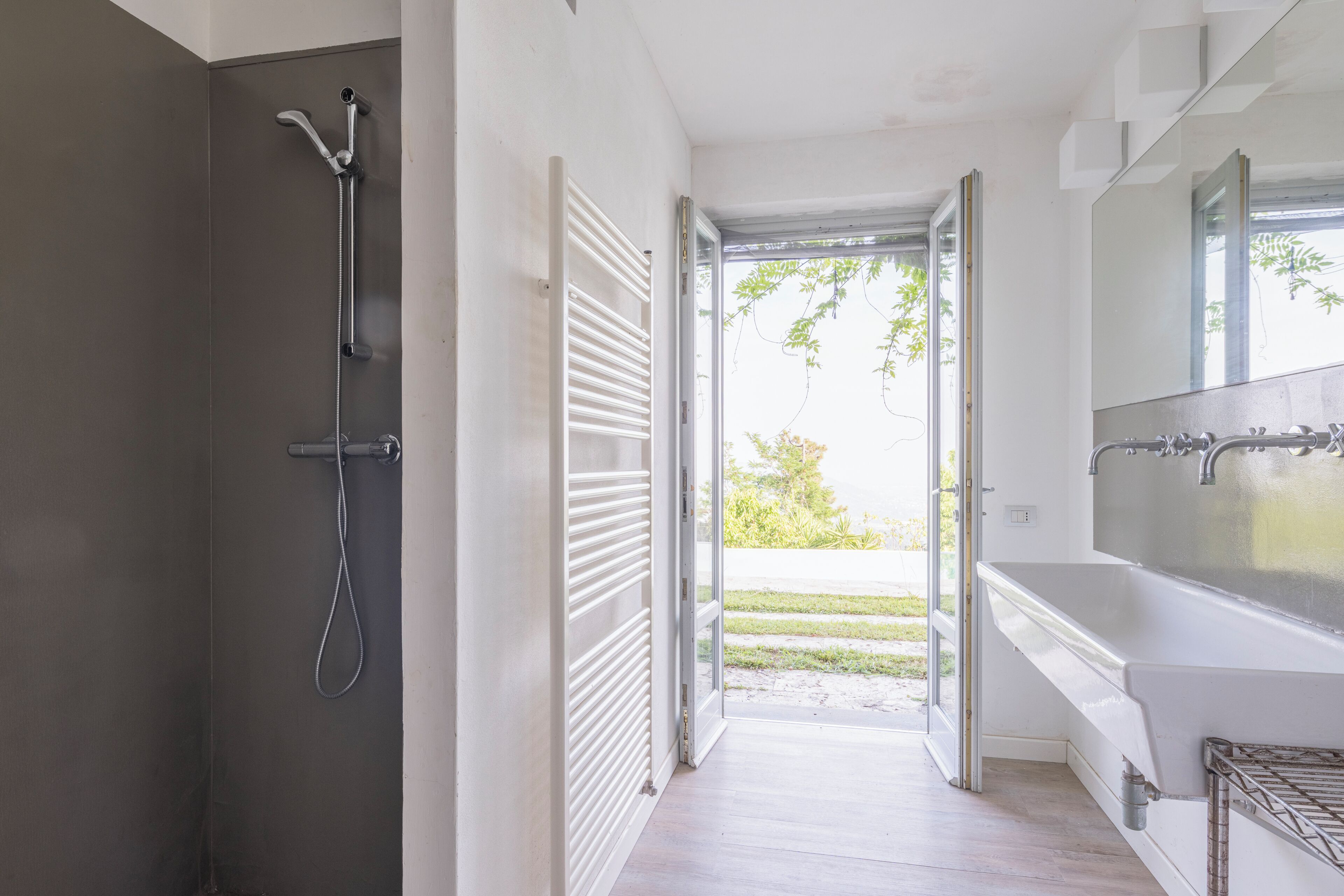 Ein modernes Badezimmer mit Dusche, großem Waschbecken und Blick durch eine offene Tür.