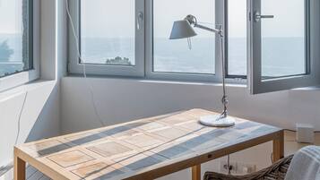 Ein Zimmer mit Holztisch, Korbstuhl und Meerblick durch große Fenster.