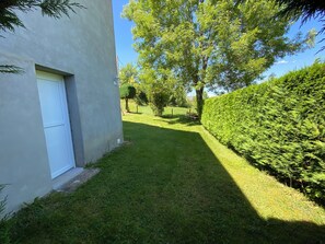 A well-maintained grassy area with a bench, a hedge, and a building with a white door.