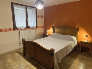 A bedroom with a wooden bed, a nightstand, a bedside lamp, a radiator, and a window with curtains.