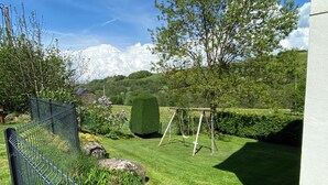 A fenced garden with a swing set, a hedge, and a lawn.