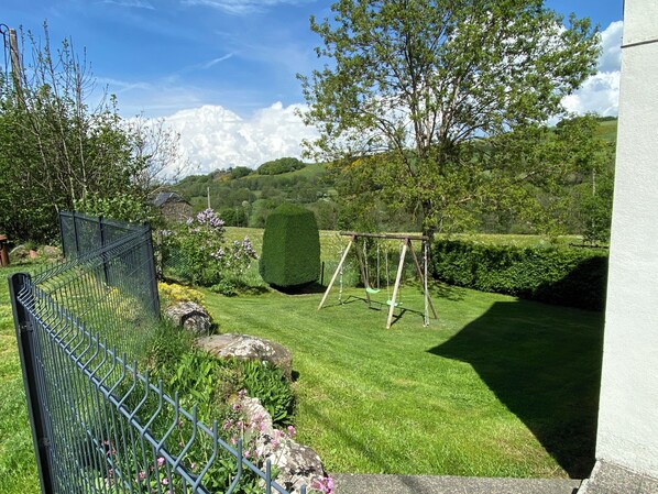 A fenced garden with a swing set, a hedge, and a lawn.