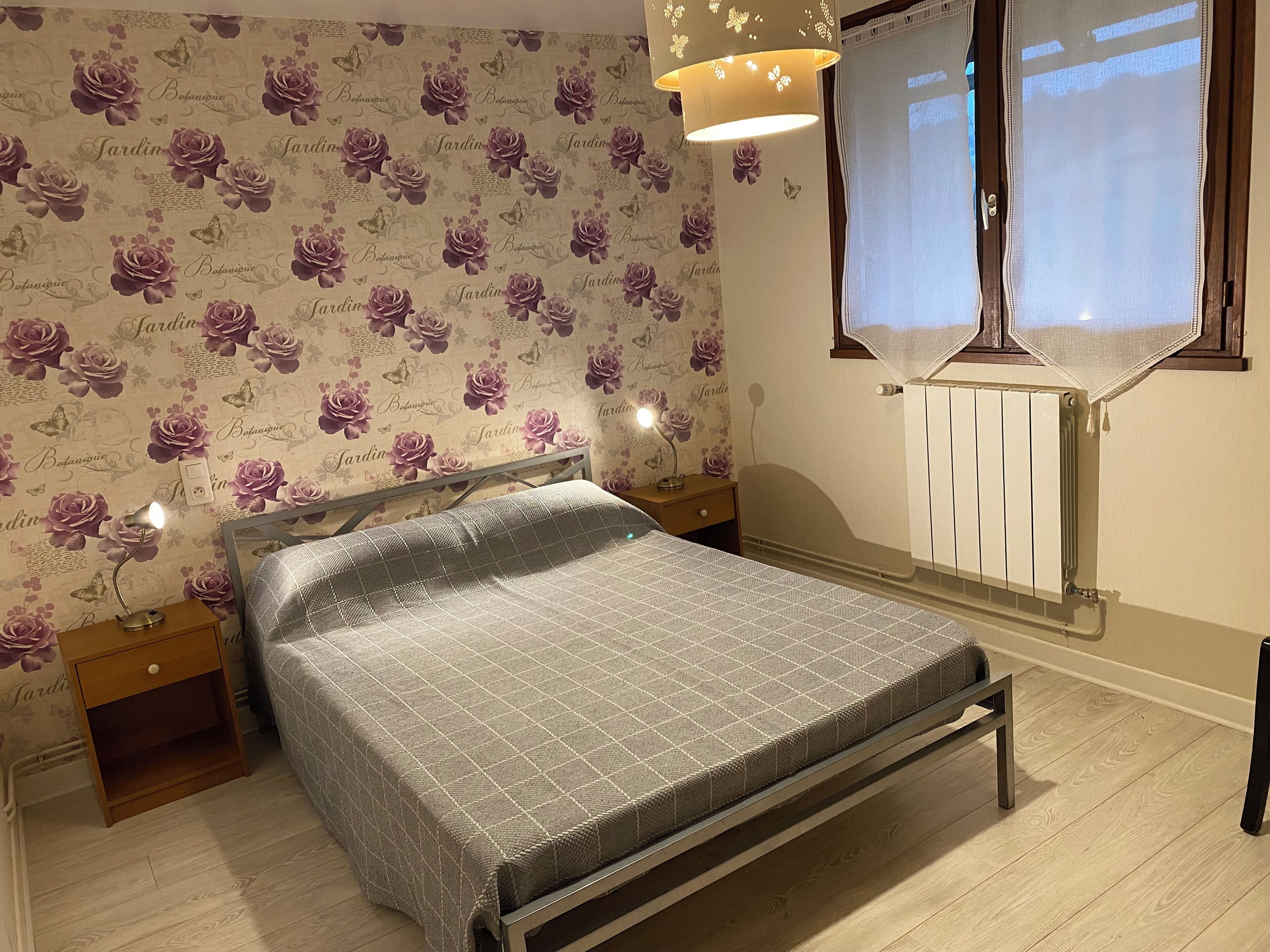 A bedroom with a bed, nightstands, a radiator, and a window with curtains.