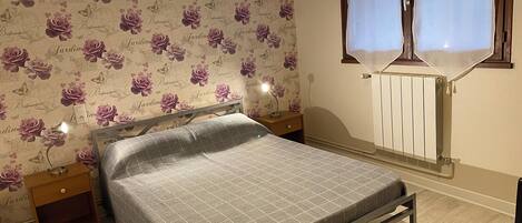 A bedroom with a bed, nightstands, a radiator, and a window with curtains.