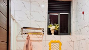 Een badkamer met toilet, handdoekhouder, douche en een raam met decoratieve lijst.