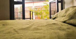 A bed with a greenish fabric, a window with a view of a red fence and greenery, and a black metal railing. - Apartments featuring Oaxaca art for 4 people (Oaxaca de Juárez)