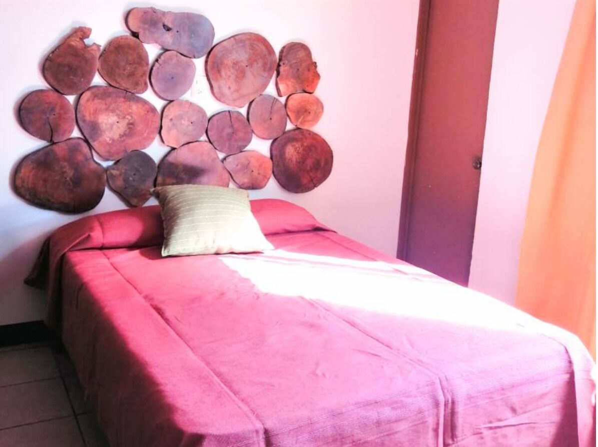 A bed with a red bedspread and a pillow, a wall with a wooden headboard, and a door to the right.